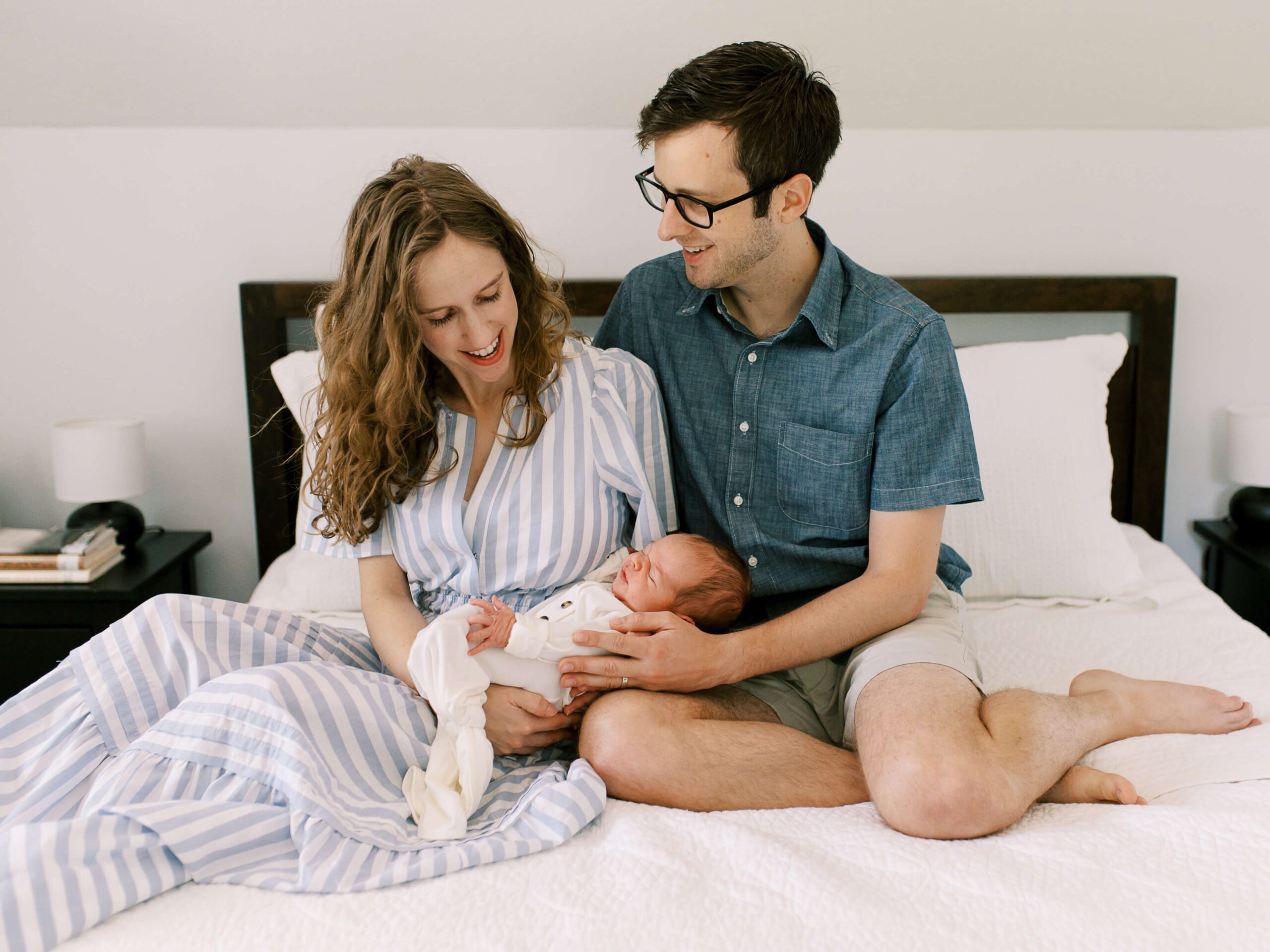mom and dad holding newborn baby on bed