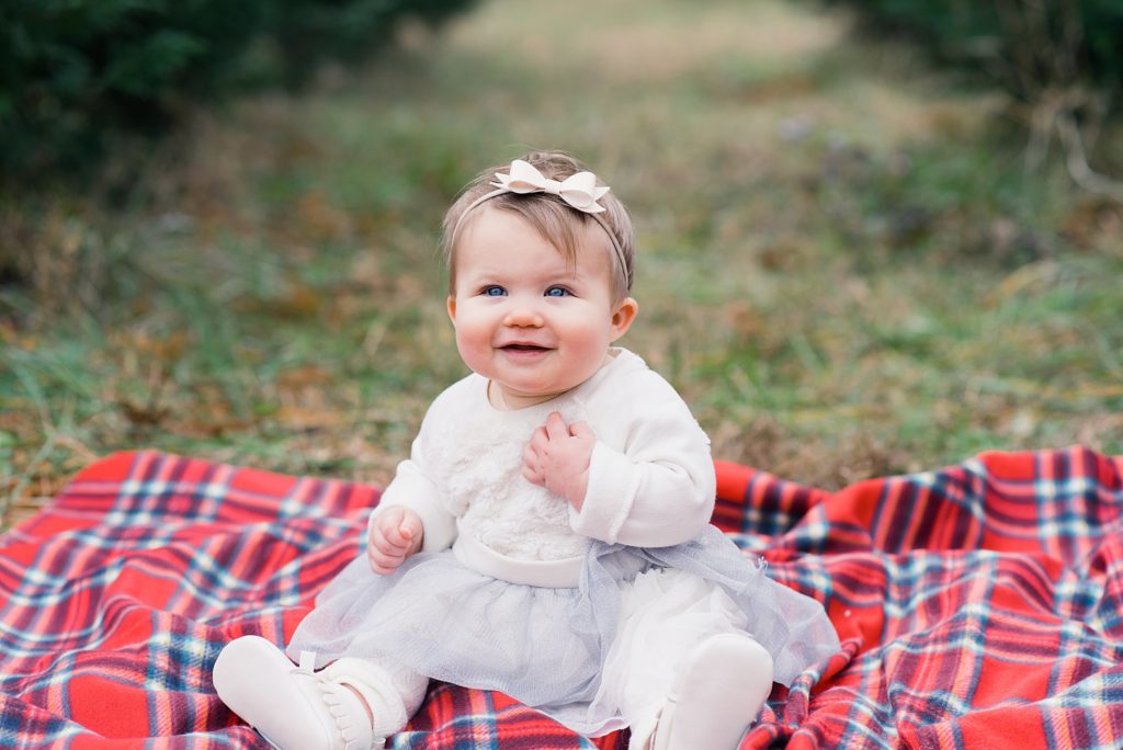 baby girl on red plaid blanket at holiday tree farm