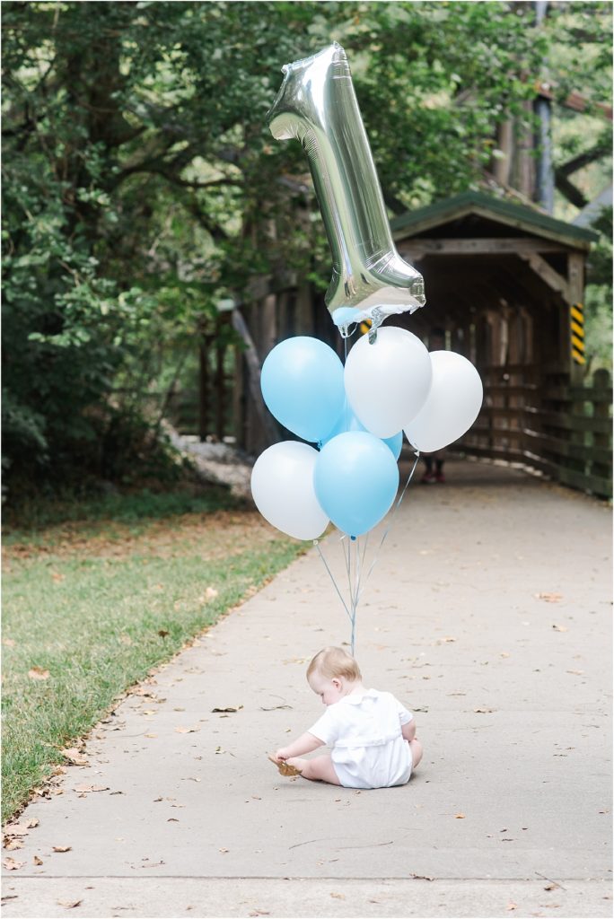 one year baby boy in park with blue and white balloons