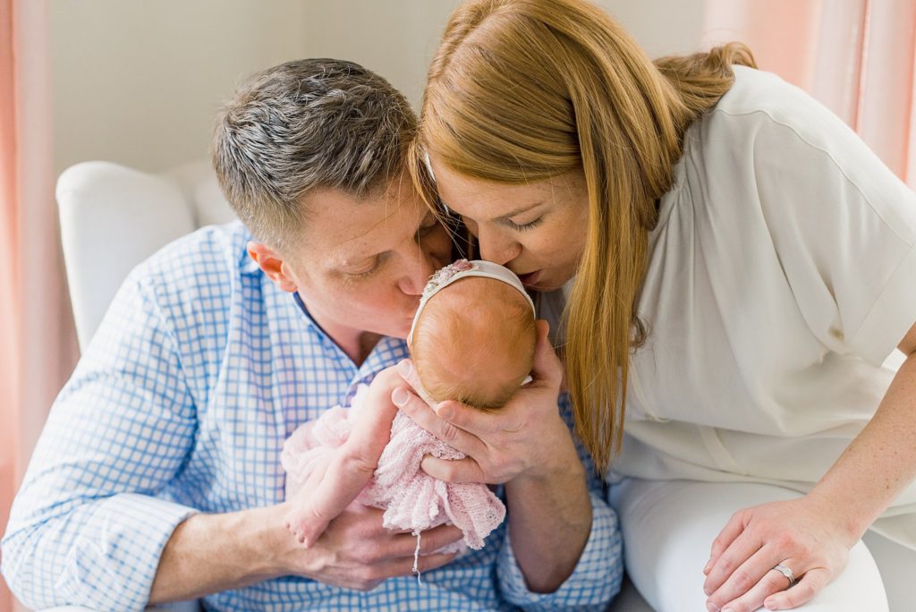 mom and dad kissing newborn baby girl