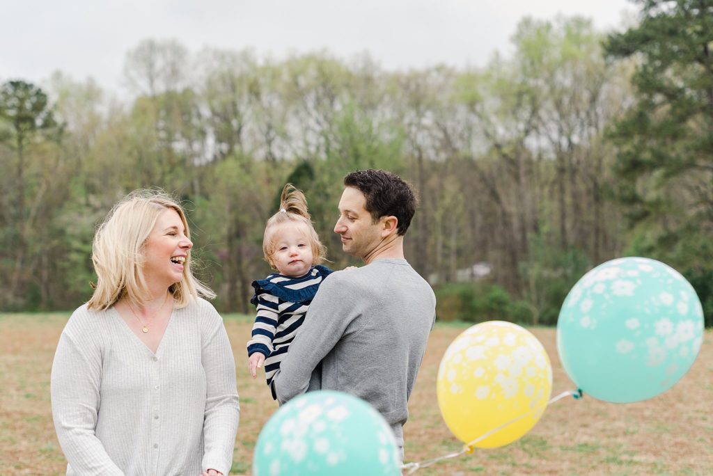one year old girl in field with balloons and mom and dad