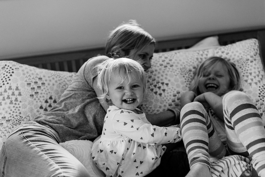 mother tickling daughters on bed