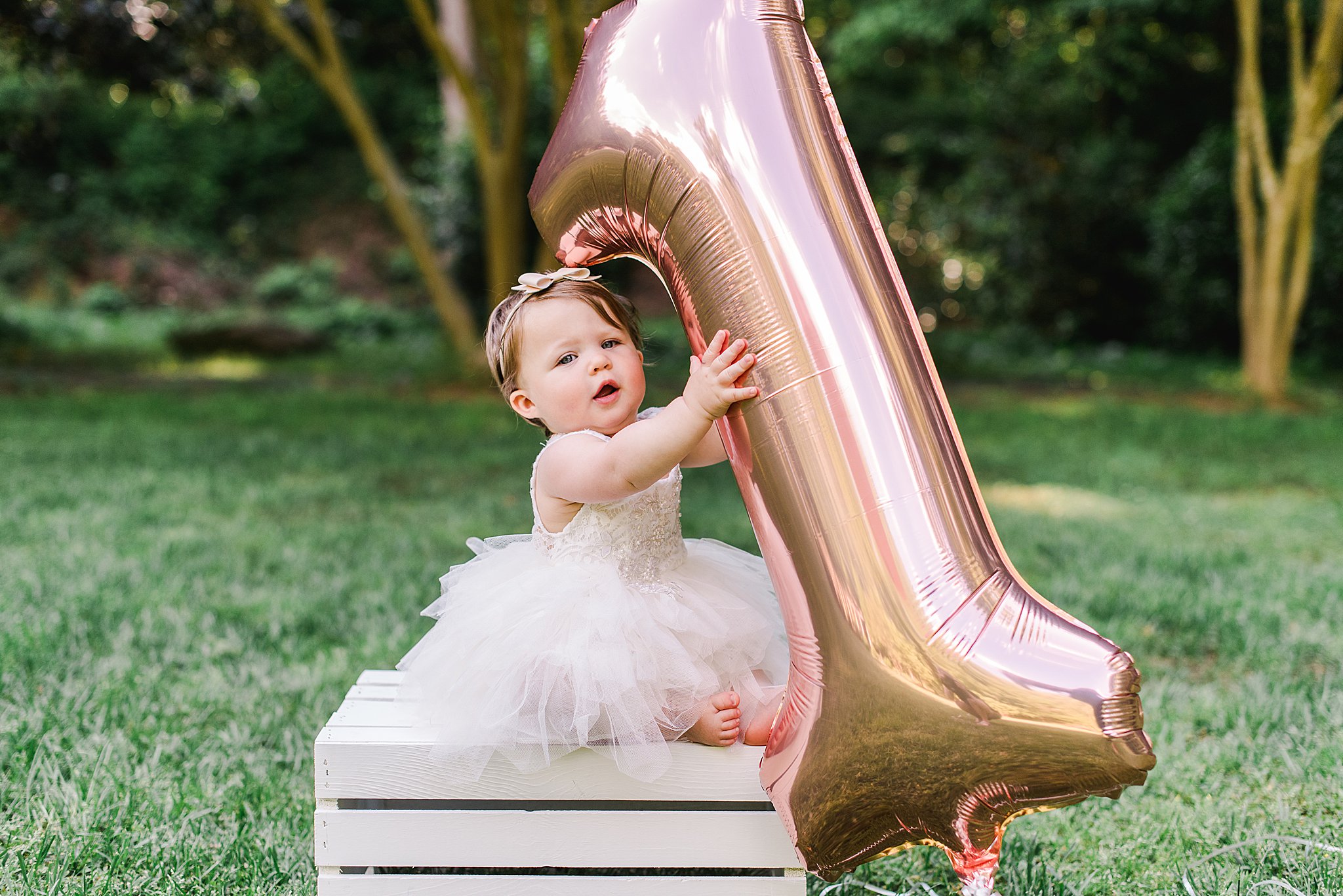 one year old girl in white dress holding pink #1 balloon