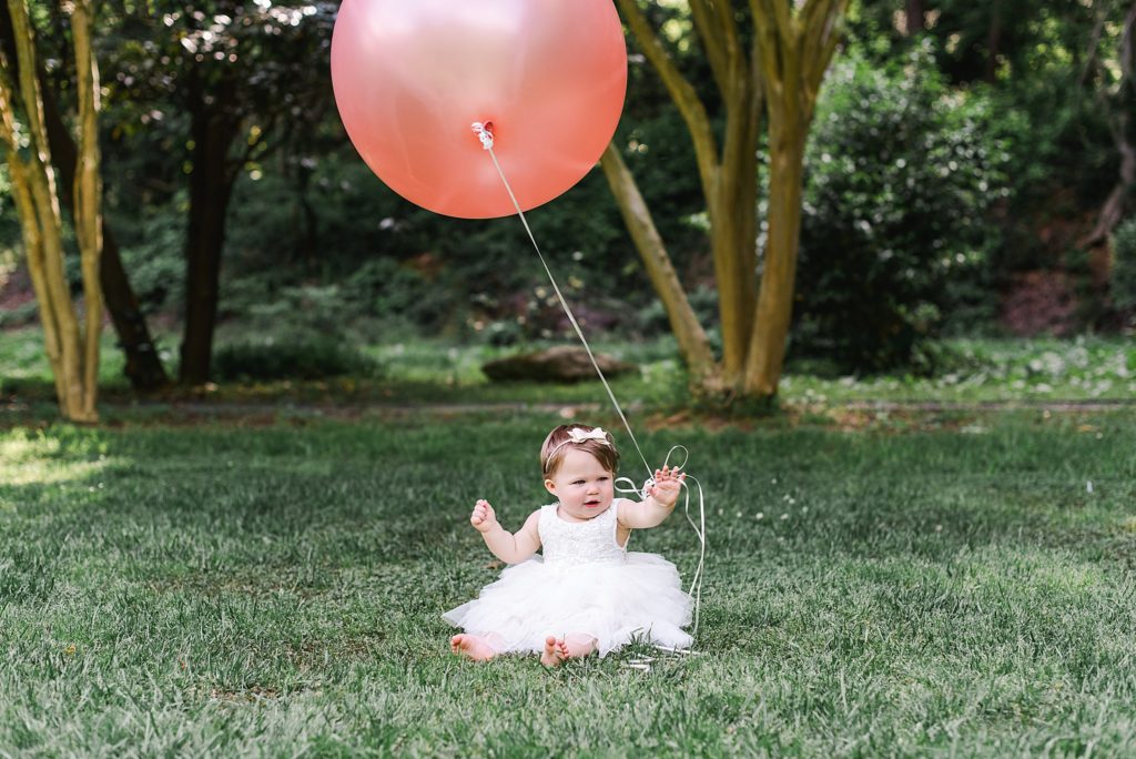 one year old girl in white dress holding pink balloon