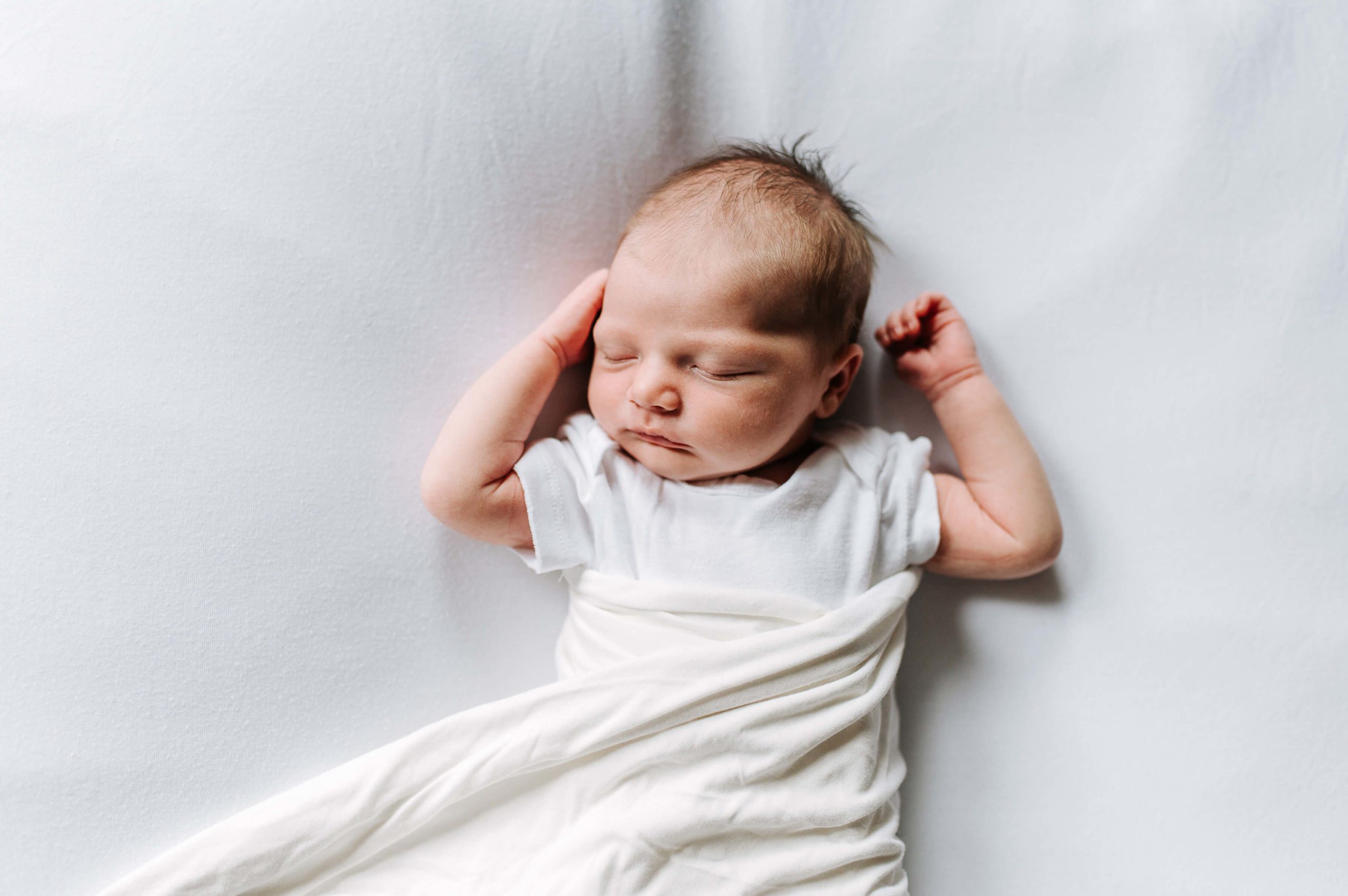 baby in white onesie asleep with arms up