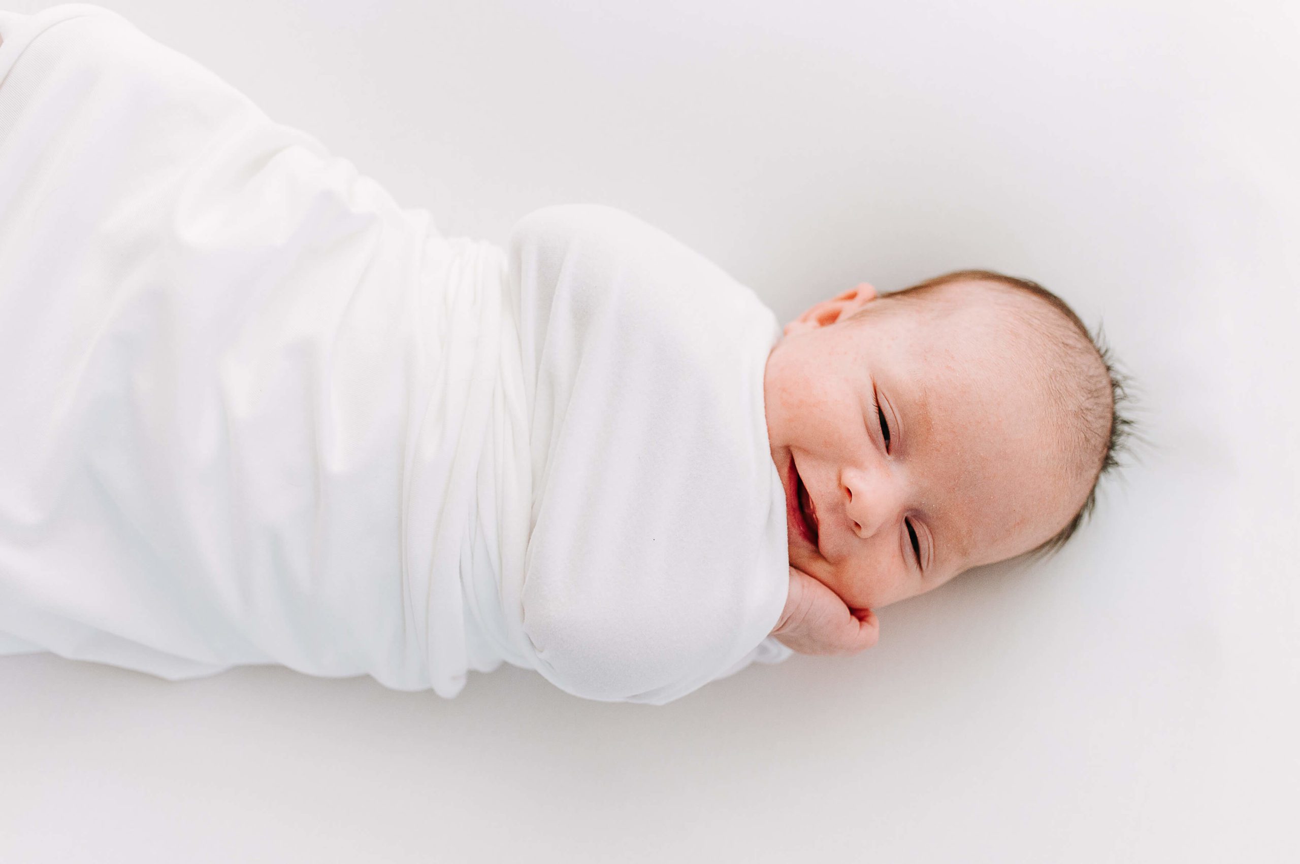 newborn baby wrapped in white swaddle smiling